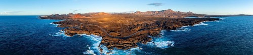 Coast with lava fields, volcanic landscape near Los Hervideros with red volcano Montaña Bermeja, in