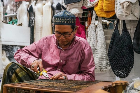 A balinese craftsman in a vibrant market setting uses tools to create crafts. The image captures