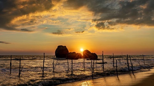 Sunset over the ocean with wooden posts and golden clouds, The Stilt Fishermen's Beach at Koggala