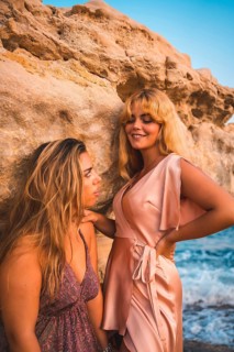 Romantic gazes of a couple of Caucasian girls with pink dresses, in a summer sunset on the beach by