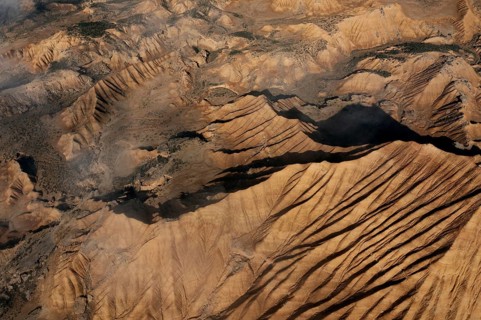 Aerial view depicting rugged desert terrain marked by dramatic ridges and gullies Sunlight casts