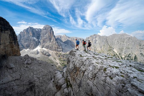 Three mountaineers on a rock in front of a picturesque mountain landscape with rocky peaks, Via
