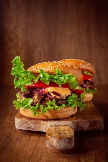 Two burgers are stacked high with fresh lettuce, tomato slices, grilled onions, and a savory sauce.
