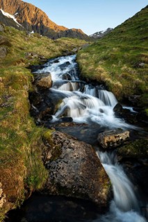 A torrent flows down the mountain. Above left the mountain Stornappstinden. Long exposure. At night