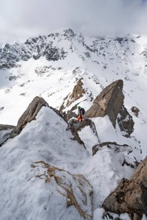 Mountaineer descending the narrow ridge of Piz Laviner, view of mountain panorama in wintry