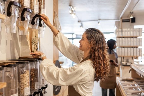 A smiling clerk fills a paper bag with grains from dispensers in an organic supermarket's bulk