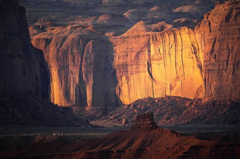 Warm golden hues illuminate the majestic cliffs of Monument Valley at sunset. The contrasting