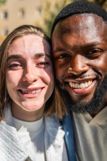 Vertical close-up portrait of a smiling multiracial young couple outdoors