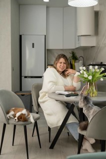 A woman in a cozy kitchen enjoys a relaxed morning with a notebook, surrounded by a sleeping dog on