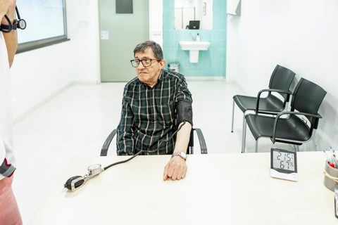 An elderly man seated at a table in a mental health residence, undergoing a routine blood pressure