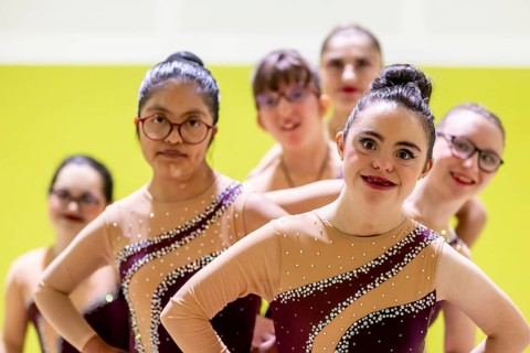 A vibrant group of disabled gymnasts in sequined costumes stand confidently, showcasing diversity