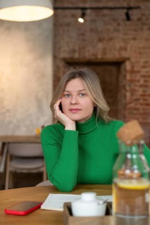 A woman in a green sweater sits at a cafe table, surrounded by a warm, cozy ambiance. With her hand