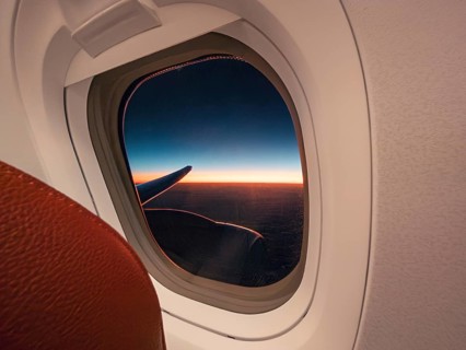 A panoramic view of a vivid sunset and aircraft wing, seen through the porthole of an airplane,
