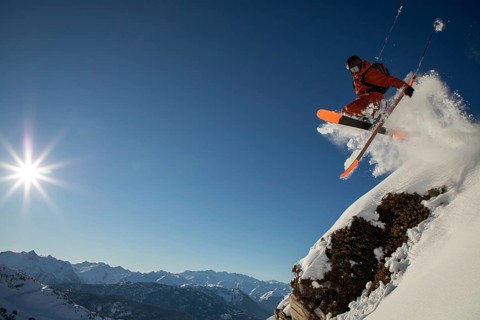 A skier wearing bright gear takes an exhilarating jump off a snowy cliff, surrounded by majestic