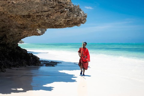 ZANZIBAR - OCTOBER 15, 2025: A Maasai man in traditional red clothing walks along a pristine white