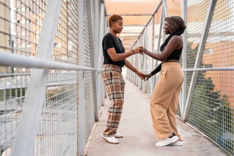 An affectionate LGBT multiethnic couple stands on a pedestrian bridge, engaged in a heartfelt