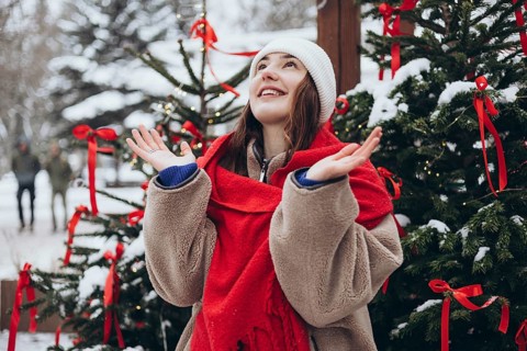 A young woman celebrates winter as she joyfully catches snowflakes near a festively decorated