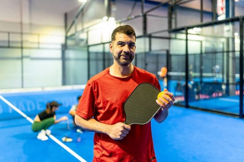 Adult male athlete wearing a red shirt holding a black carbon paddle and yellow ball while standing