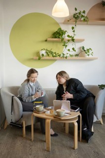 Two women engage in conversation in a cozy cafe setting. Surrounded by coffee, pastries, and