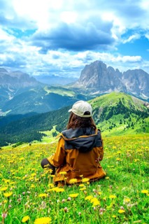 Hiker relaxing in a meadow of yellow flowers admiring the odle mountains in the italian dolomites