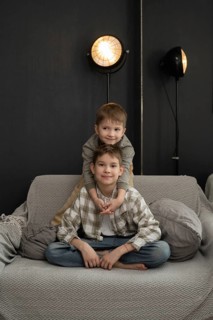 Two children share a joyful moment at home, with one sitting and the other playfully resting on his