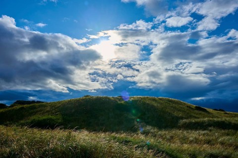 Grassy hills under dramatic clouds and sunshine, Seahouses, Northumberland, England, United Kingdom