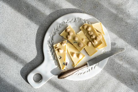 Top view of a sliced white chocolate bar with nuts, accompanied by a rustic knife on a decorative