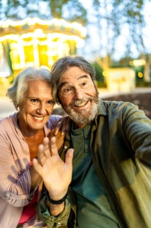 Vertical close-up personal perspective photo fo a happy modern senior couple waving taking selfie