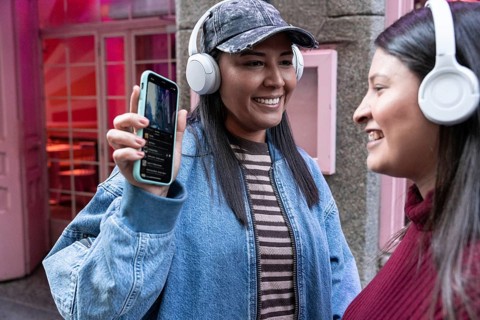 A joyful Latin lesbian couple, wearing headphones, shares a moment of connection while listening to