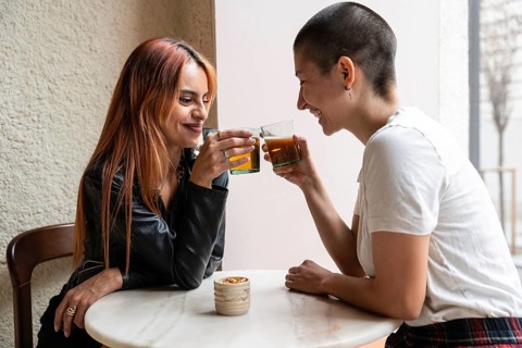 A joyful lesbian couple sharing a drink at a round table in a cozy cafe, engaging in friendly
