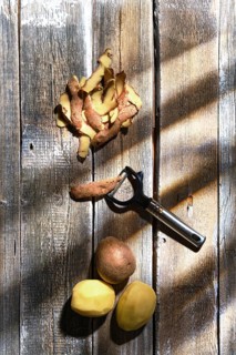 Overhead view of fresh potatoes and potato peelings with a knife on a table