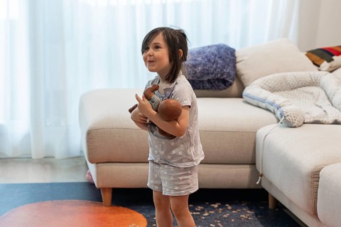 A young girl joyfully embraces her doll in a cozy living room, symbolizing love and innocence. The