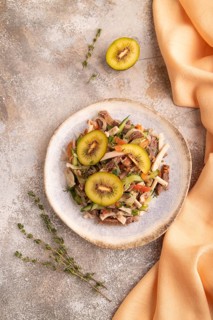 Meat salad with beef kiwi and vegetables on brown concrete background and orange linen textile. top
