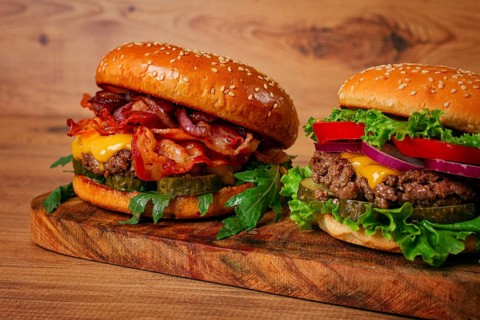 Two burgers with beef patty, fried bacon, cheddar cheese, tomatoes, homemade, no people