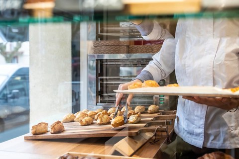 Baker wearing a white uniform carefully placing warm, golden pastries from a baking tray onto a