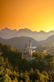 Neuschwanstein Castle in a mountainous scenery at a golden sunset, embedded in green forests,