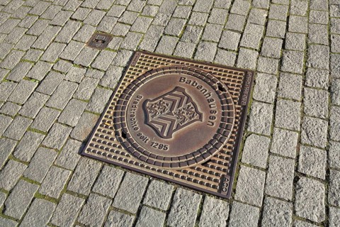 Square manhole cover with city coat of arms and date for historical city rights, paving stones,