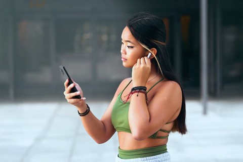 A young Chinese woman wearing a green top and wristbands, holding a smartphone and listening to