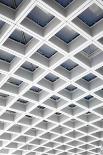 A modern airport ceiling features a geometric grid of skylights, creating a pattern of light and