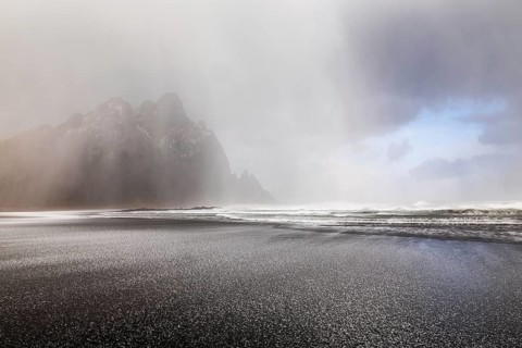 Sleet on black lava sandy beach against mountain backdrop, sea, winter, Stokksnes, Vestrahorn,