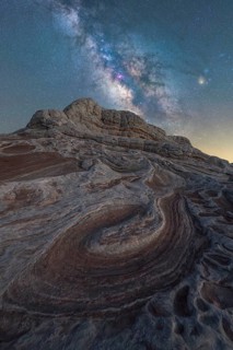 The Milky Way sparkles in a clear night sky over the dramatic and swirling sandstone formations of