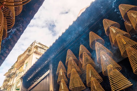 From below large incense spirals emit smoke beneath aged balconies in a Taoist and Chinese Buddhist