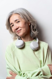 Asian Chinese senior woman with gray hair, wearing a light green sweater and white headphones