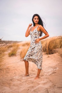 Portrait of a Caucasian brunette stroking her hair in a white flowered dress, in the sand on the