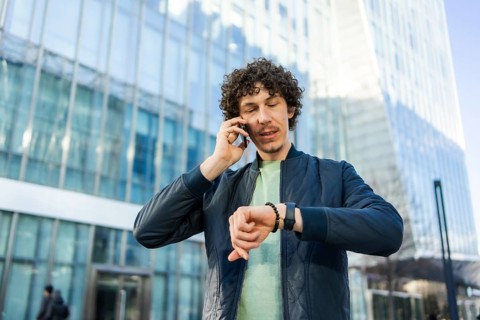 A businessman stands in front of a glass building, talking on his smartphone while checking the