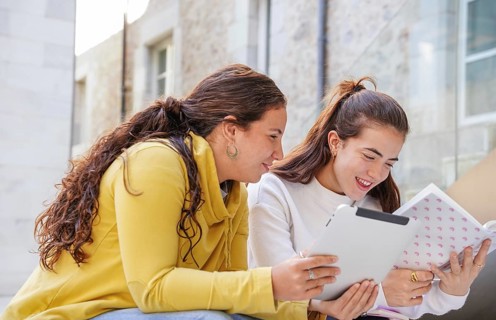 Two students enjoy a study session outside on a sunny day, using a tablet and a notebook They