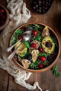 A vibrant salad featuring fresh figs, avocado, cherries, and blackberries on a bed of arugula,