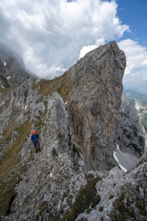 Mountaineer with helmet on a narrow hiking trail on a rocky ridge, ascent to the Maukspitze, clouds
