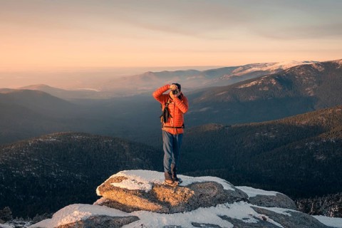 A photographer stands atop a snow-dusted peak at Siete Picos, Guadarrama Mountains, capturing the