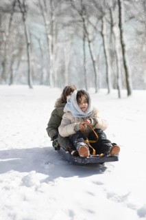 Two children joyfully sled through the snow-covered woods at Sierra Nevada Ski Resort in Granada.